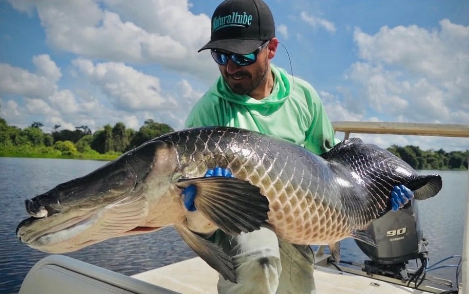 Man holding large fish on boat under cloudy blue sky at Arapaima Lodge, Bolivia