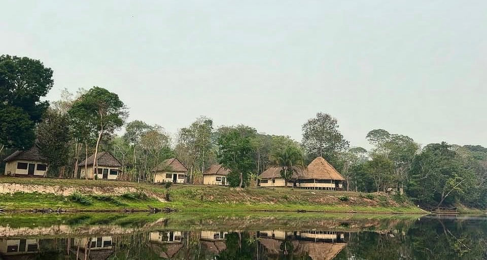 Scenic view of a row of huts with a reflective water body and trees in the background.