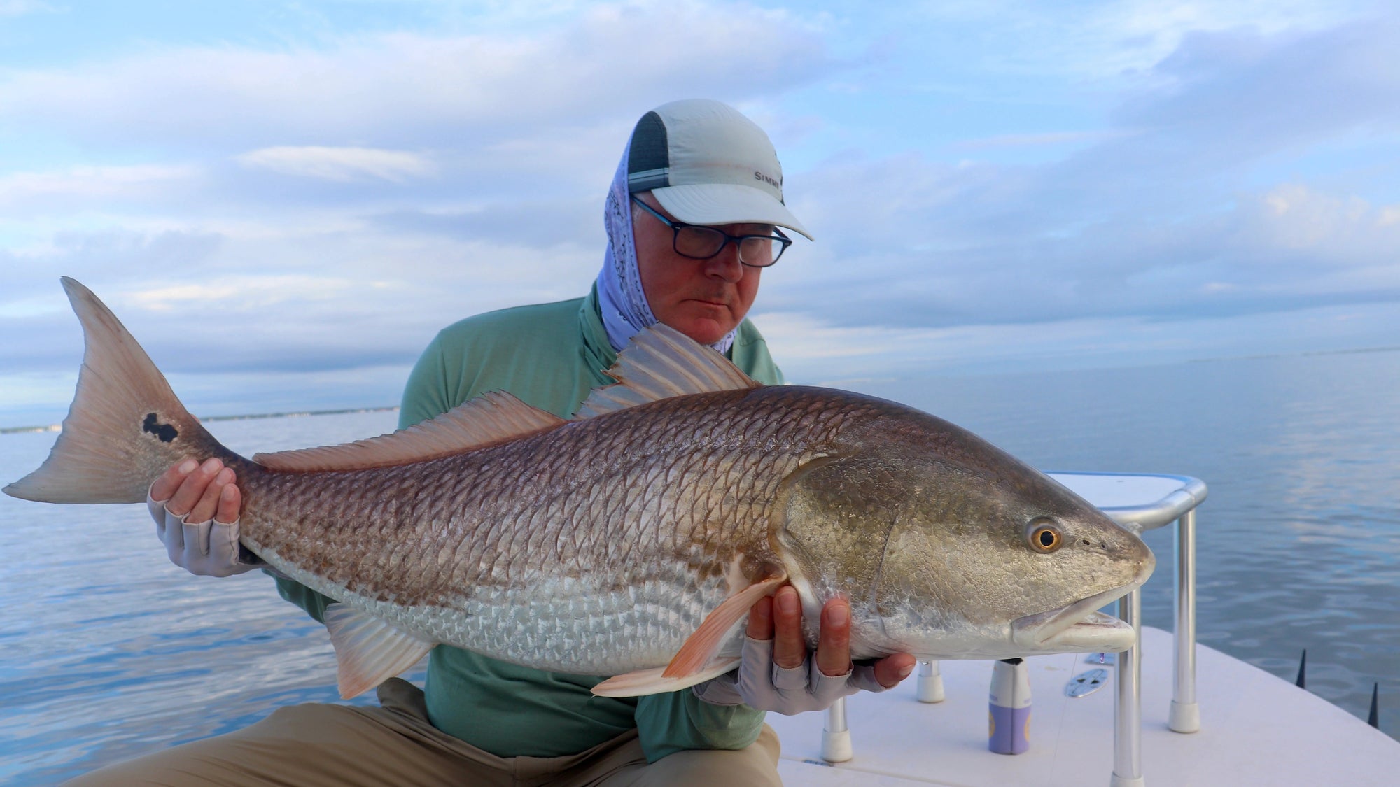 Man holding a large redfish on a boat with a clear sky background
