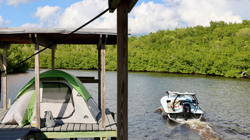 Tent on a wooden platform overlooking a body of water with a boat in the background.